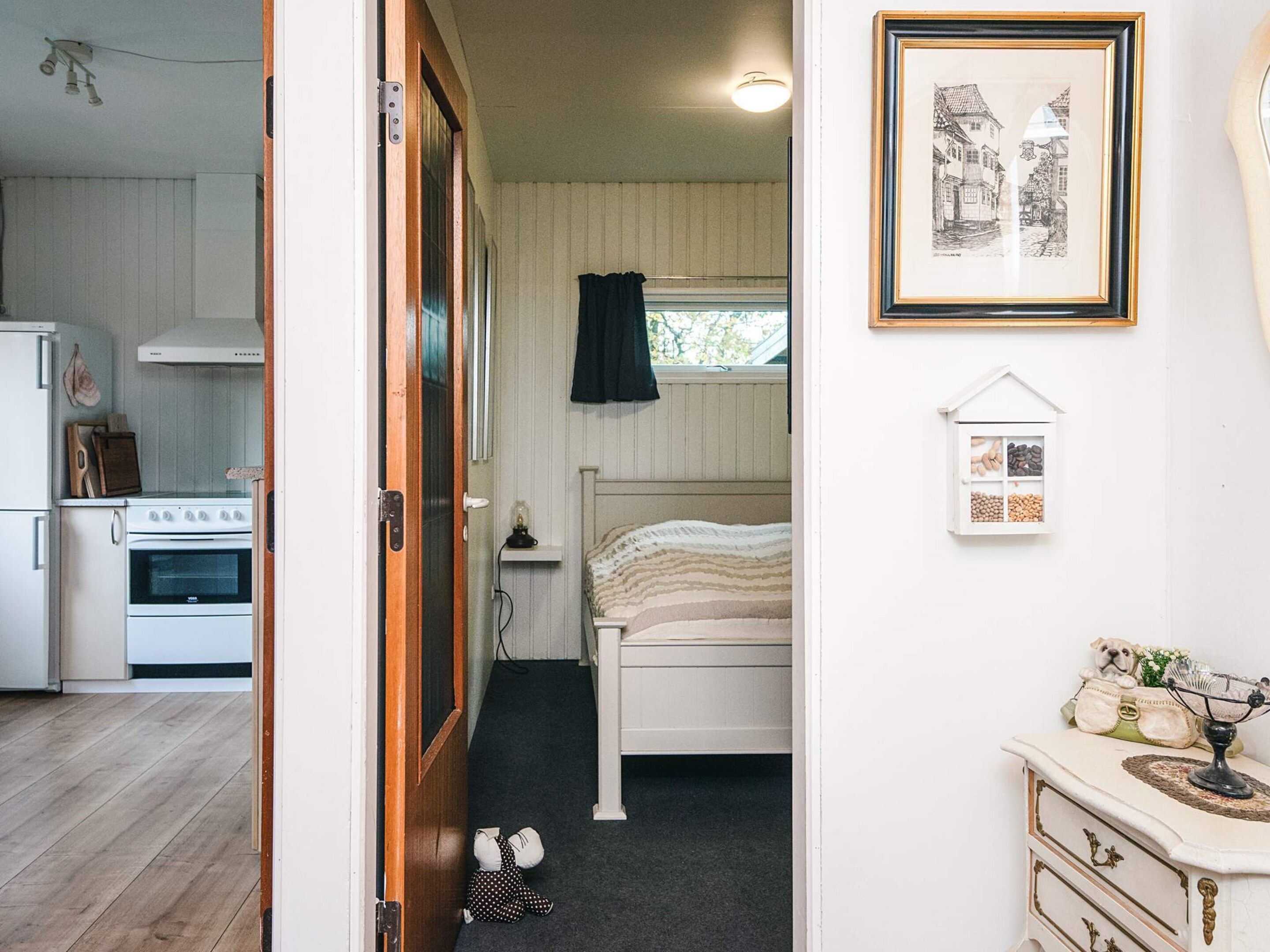 Una habitación pequeña con cama, mesita de noche, un cuadro enmarco y un armario blanco.