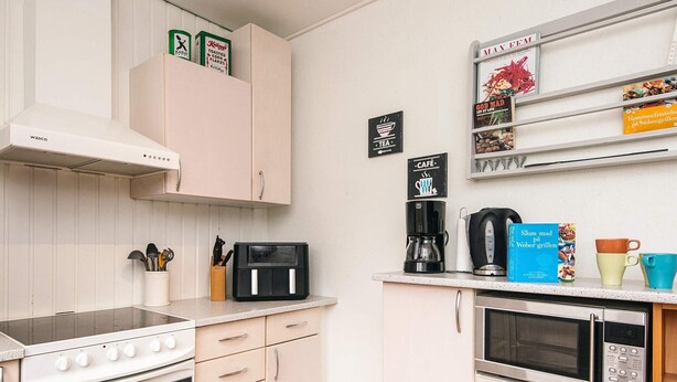 A modern kitchen with a stove, oven, microwave, and coffee maker. There are cabinets, a shelf with books, and a coffee cup on the counter. - 6 Person Holiday Home in Orsted (Ørsted)