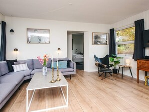 A modern living room with a grey sofa, a coffee table, and a dining area with a chair and table. - 6 Person Holiday Home in Orsted (Ørsted)