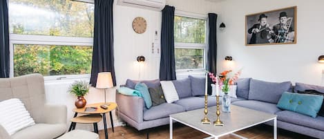 Uma sala de estar moderna com um sofá cinzento, uma mesa de centro, uma mesinha lateral com abajur e um relógio de parede.