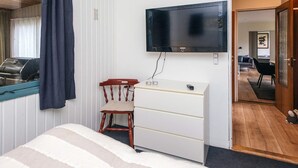 A bedroom with a bed, a wooden chair, a white dresser, a flat-screen TV mounted on the wall, and a window with curtains. - 6 Person Holiday Home in Orsted (Ørsted)