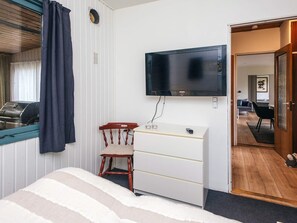 A bedroom with a bed, a wooden chair, a white dresser, a flat-screen TV mounted on the wall, and a window with curtains. - 6 Person Holiday Home in Orsted (Ørsted)