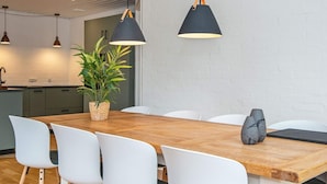 Un espace de salle à manger moderne avec une table en bois, des chaises blanches et deux lampes suspendues.