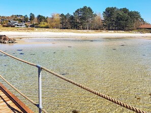 A clear view of a beach with a wooden walkway leading to the water, surrounded by trees and houses in the background. - 6 Person Holiday Home in Ebeltoft (Ebeltoft)