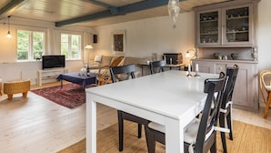 Uma sala de estar espaçosa com uma mesa e cadeiras brancas, uma televisão e um espaço de jantar com um tapete vermelho.