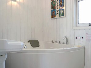 A white bathtub with a green towel, a window with a view, and a wall with colorful artwork. - 8 Person Holiday Home in Saltum (Saltum)