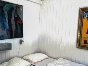 A single bed with white bedding and pillows, a wall-mounted shelf, and two artworks. - 8 Person Holiday Home in Saltum (Saltum)