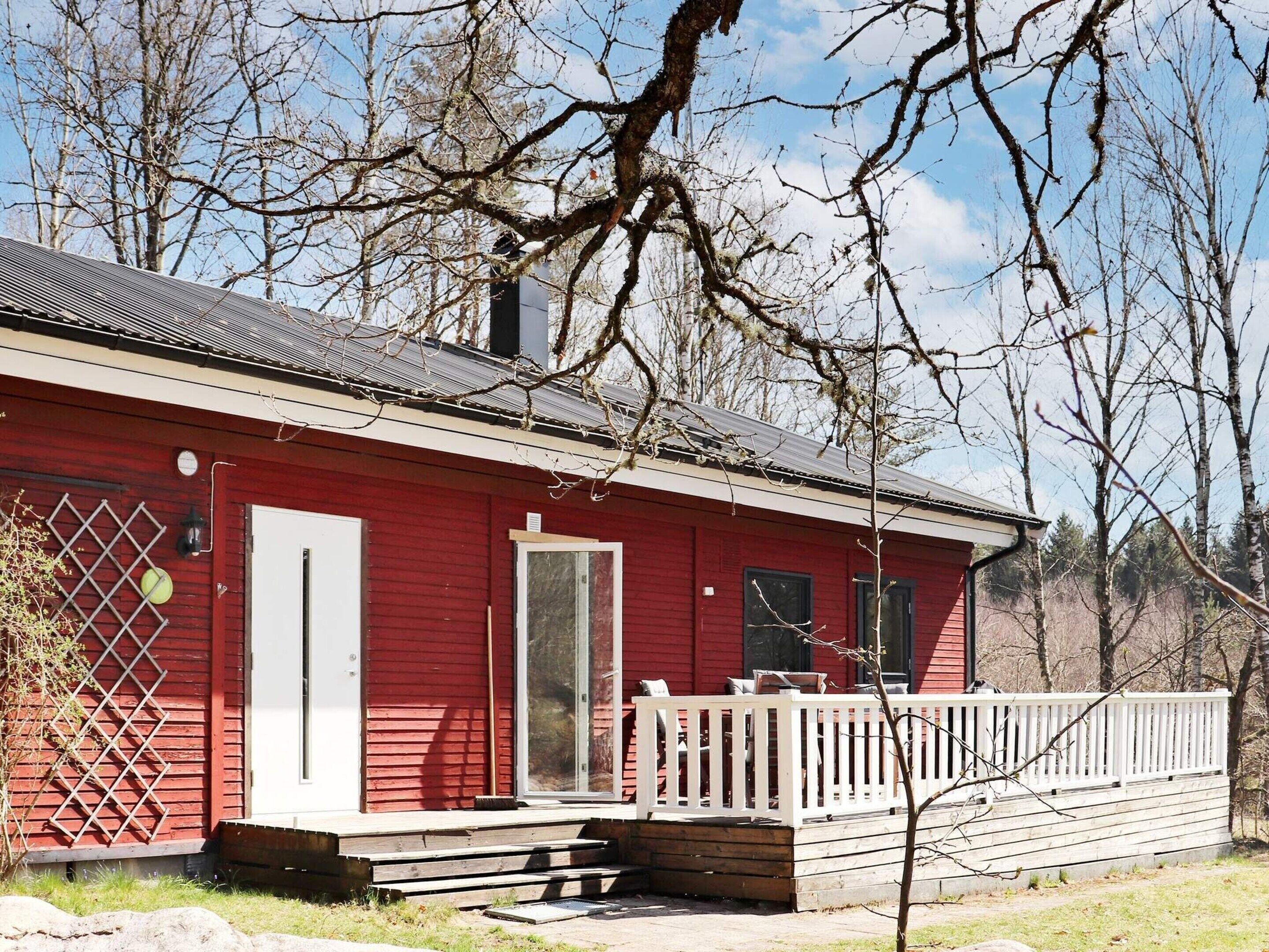 A red wooden building with a white door, a small porch, and a metal fence.