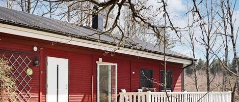 A red wooden building with a white door, a small porch, and a metal fence.