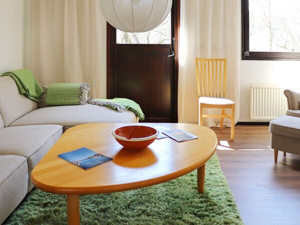 A living room with a sofa, a wooden coffee table, a green rug, a chair, and a window with a view of trees. - 4 Star Holiday Home in Knared (Knared)