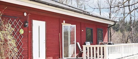 Une cabane rouge avec une porte blanche, un petit porche et une cheminée.