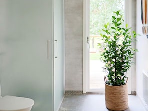 A bathroom with a toilet, a door, and a potted plant near a sliding glass door.