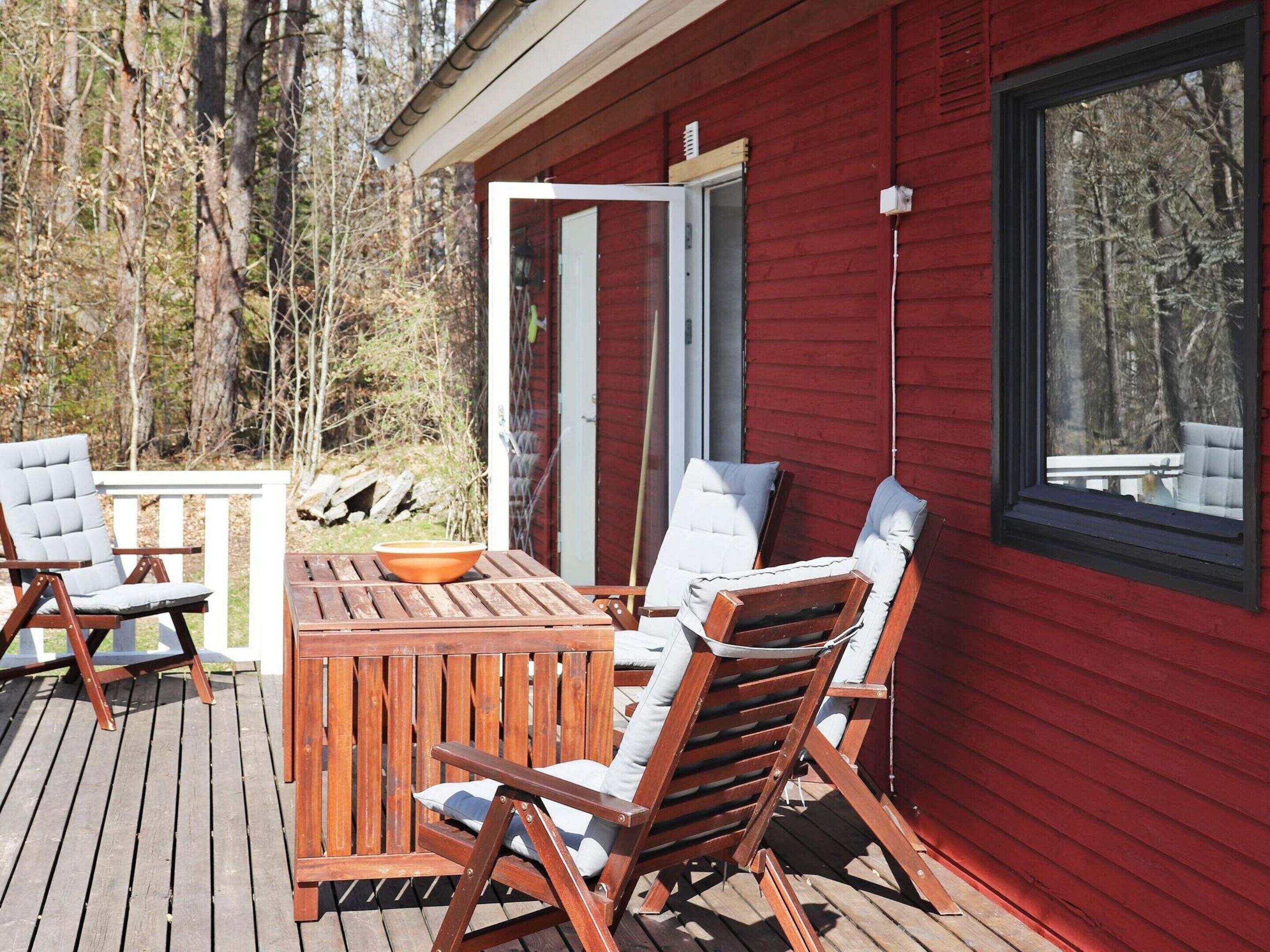 A wooden deck with a table and chairs, a window, and a view of trees.