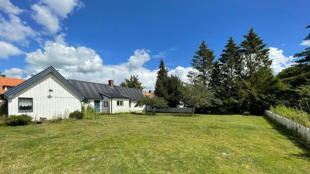 A white house with a grey roof, surrounded by a well-maintained lawn and tall trees. - 4 Person Holiday Home in Everod (Everöd)
