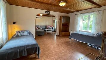 A room with two beds, a sofa, a wooden ceiling, and a window with curtains.