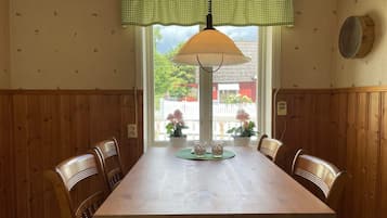 A dining area with a wooden table and chairs, a hanging lamp, and a window with a view of the outside.