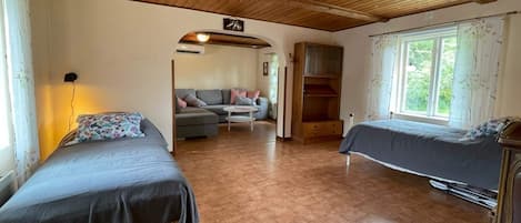 A room with two beds, a sofa, a wooden ceiling, and a window.