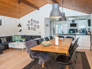 A modern kitchen with a central island, a dining area with a wooden table and black chairs, and a living room with a dark sofa and a white coffee table.