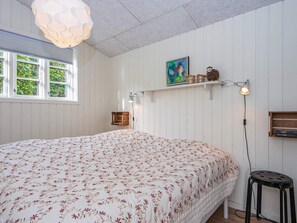 A bedroom with a floral bedspread, a hanging light fixture, a shelf with decorative items, and a window with greenery outside. - Panoramic Water View - By Traum Ferienwohnungen (Kolding)