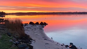 En stilla sjö vid solnedgången, med en stenig strand och träd i fjärran.