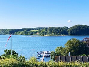 A lakeside view with boats docked, a flagpole, and a house on the shore. - Panoramic Water View - By Traum Ferienwohnungen (Kolding)