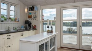 Ett kök med vita skåp, en kaffemaskin och utsikt över en sjö genom stora glasdörrar.