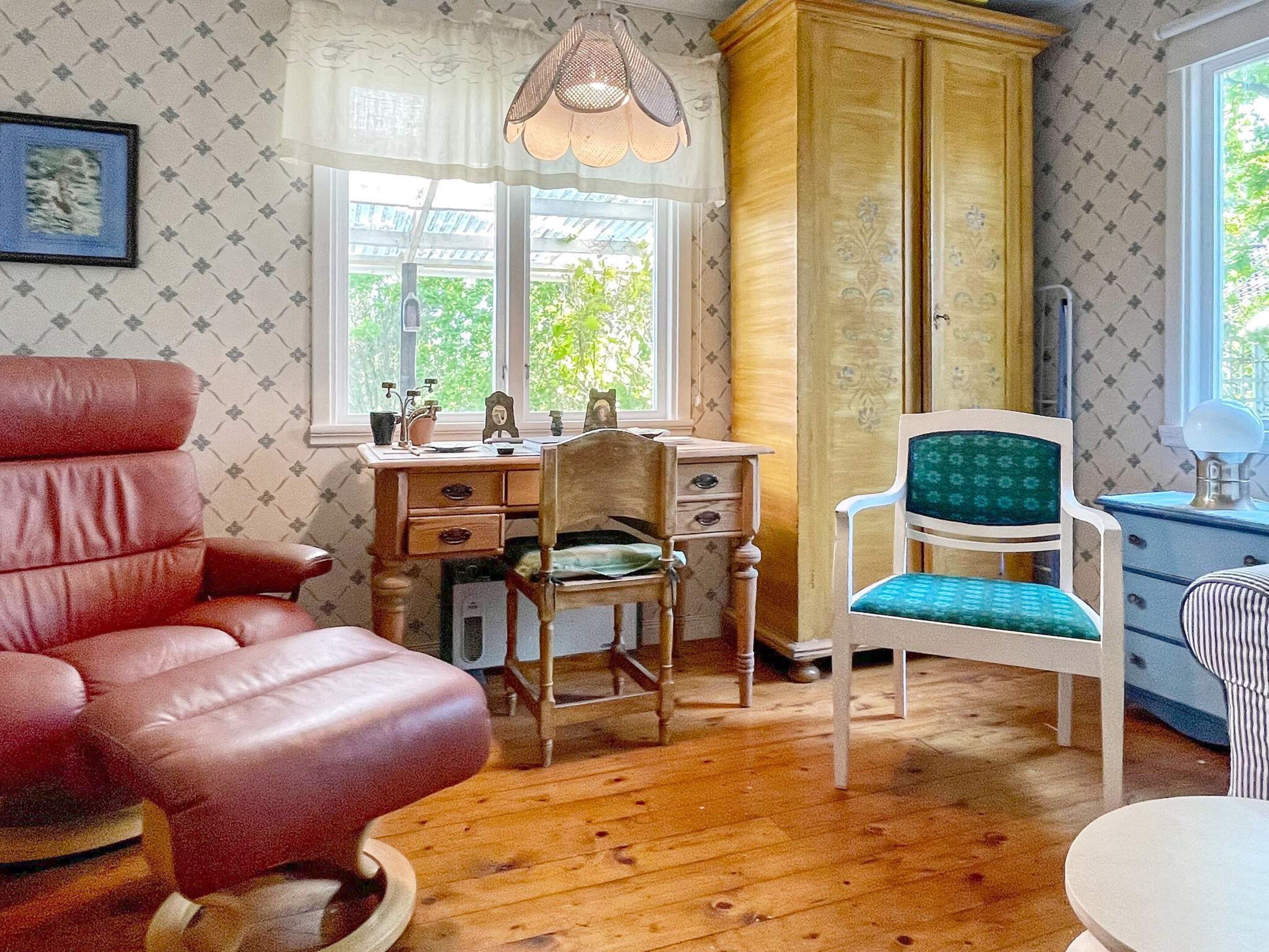 A room with a wooden desk, a red leather chair, a green upholstered chair, and a wardrobe.