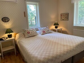 A bedroom with a bed, two nightstands, a lamp, a clock, and a window with a view of trees.