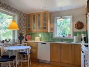 A kitchen with wooden cabinets, a green backsplash, a window with a view, and a dining area with a table and chairs. - 4 Star Holiday Home in Rockneby (Rockneby)