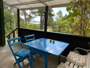 A covered patio with a blue table and chairs, a white bench, and a view of trees and a body of water. - 4 Star Holiday Home in Rockneby (Rockneby)
