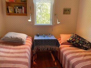 A small room with two beds, a window, a shelf with books, and a table with a patterned tablecloth. - 4 Star Holiday Home in Rockneby (Rockneby)