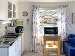 A compact kitchen with a microwave, kettle, and coffee maker. A wooden table with a lamp is near a window with floral curtains. - 4 Star Holiday Home in Bengtsfors (Bengtsfors)