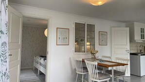 Une pièce compacte comprenant un lit, une table à manger avec des chaises, un coin cuisine et une estampe botanique encadrée accrochée au mur.