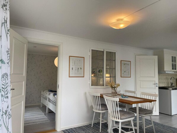 Una habitación con cama, una mesa de comedor con sillas, una zona de cocina y un ventanal con vidrio esmerilado.