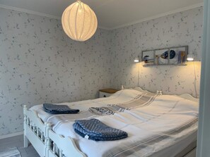 A bedroom with a bed, a hanging light fixture, a bedside table, and a wall-mounted shelf with decorative items.
