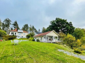 A residential area with two houses, one with a balcony and the other with a porch. There is a grassy lawn with a few scattered leaves. - 4 Star Holiday Home in Bengtsfors (Bengtsfors)