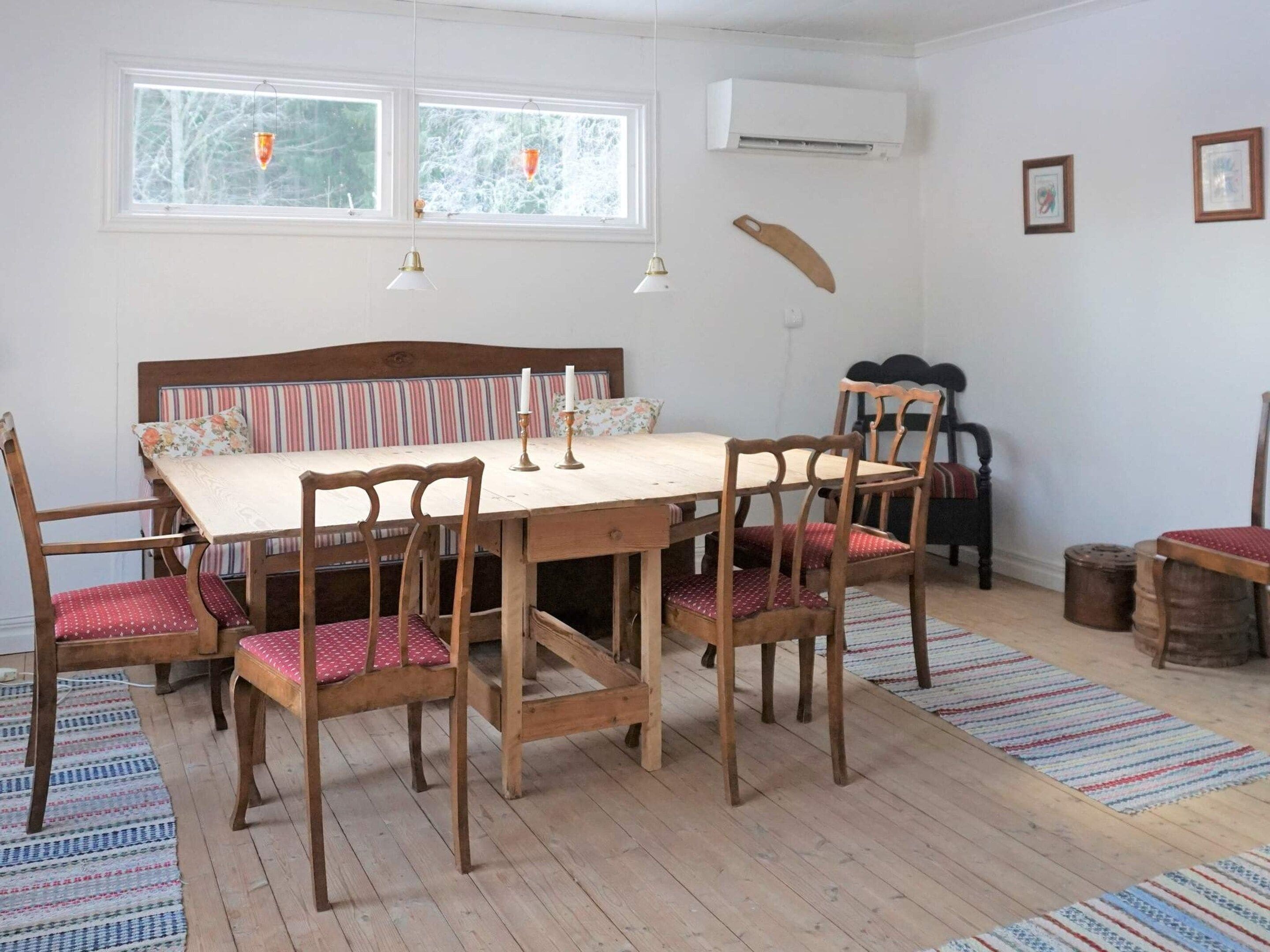 A dining area with a wooden table and chairs, a striped bench, and a window with curtains.