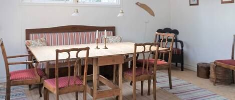 A dining area with a wooden table and chairs, a striped bench, and a window with curtains.
