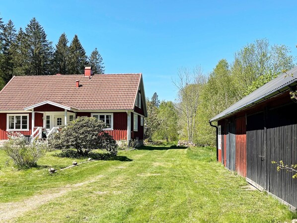 Ein rotes Haus mit Ziegeldach, ein hölzernes Nebengebäude und ein Rasenstück.
