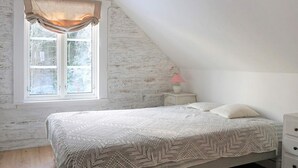A bedroom with a sloped ceiling, a bed with a patterned blanket, a nightstand with a lamp, and a window with curtains. - 4 Star Holiday Home in Hallabro (Hallaröd)