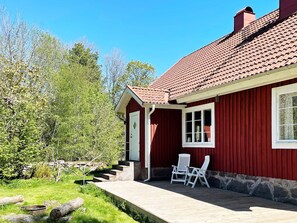 A red wooden house with a tiled roof, a front door, and a small porch with two white chairs. - 4 Star Holiday Home in Hallabro (Hallaröd)