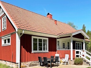 Ein rotes Holzhaus mit einem Ziegeldach, einer Veranda mit weißen Geländern und einer Treppe zum Eingang.