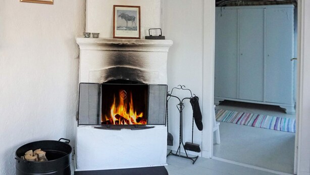 A fireplace with a fire, a black bucket of wood, and a striped rug on the floor. - 4 Star Holiday Home in Hallabro (Hallaröd)