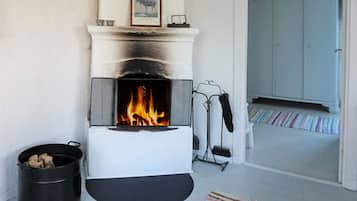 A fireplace with a fire, a black bucket of wood, and a striped rug on the floor.
