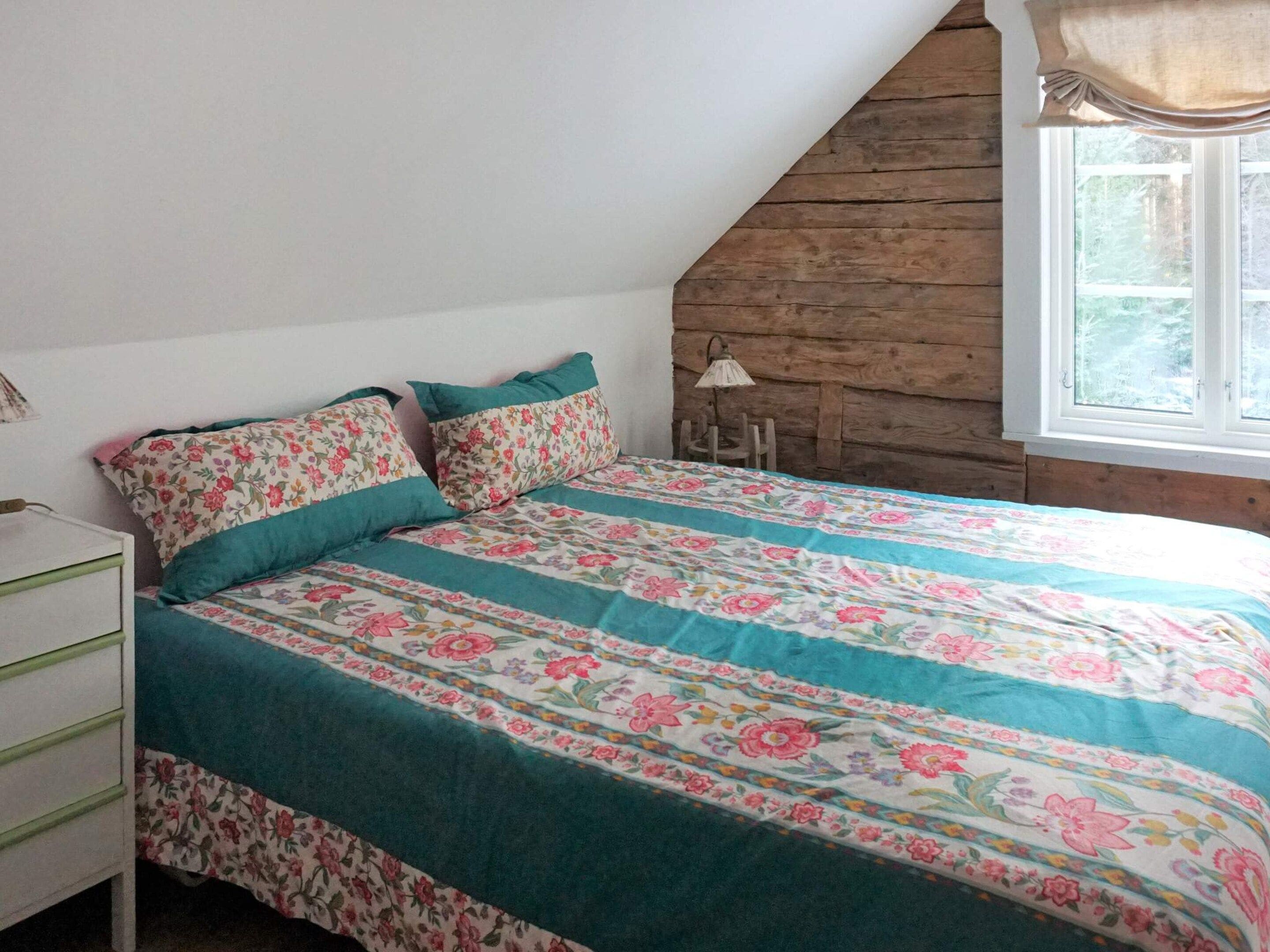 Une chambre à coucher avec un lit, une table de chevet, une lampe et une fenêtre donnant sur des arbres.