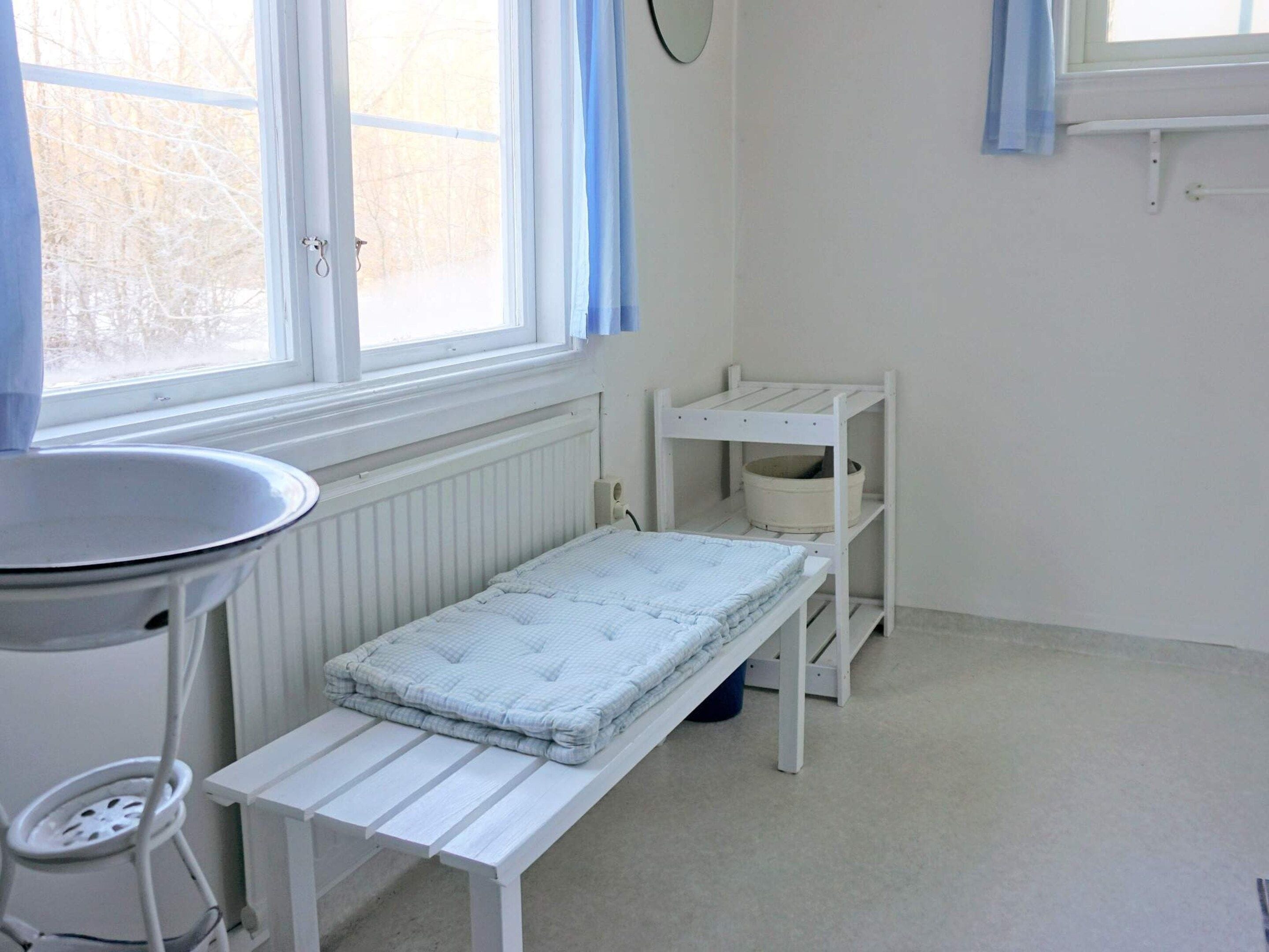 A small, bright room with a window, a radiator, a white table, and a shelf unit.