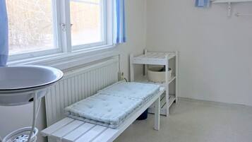 A small, bright room with a window, a radiator, a white table, and a shelf unit.