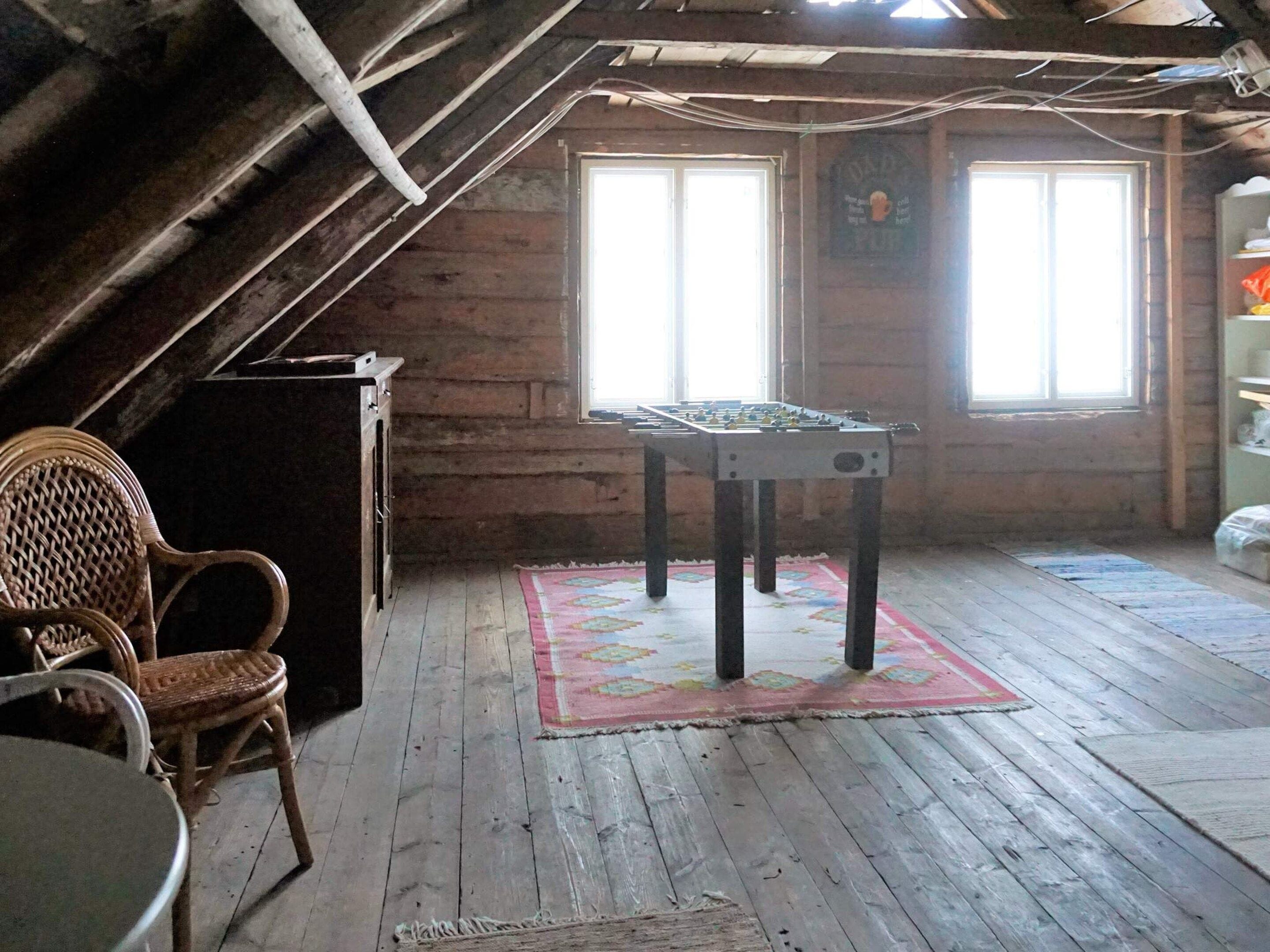 Una habitación con una mesa de madera, dos sillas, una mesa de futbolín y un ventanal con un cartel.