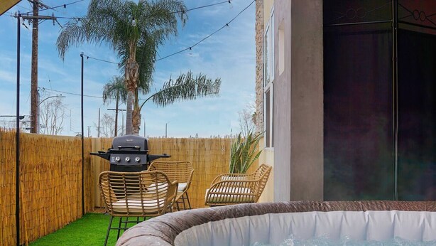 A hot tub with wicker chairs, a grill, and a bamboo fence in a backyard setting. - South Bay Sanctuary (Lawndale)