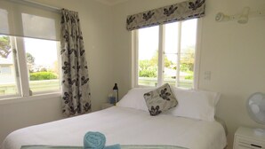 A neatly made bed with a blue towel, a pillow with a floral pattern, and a bedside lamp. - Hibiscus Hideaway (Karikari Peninsula)
